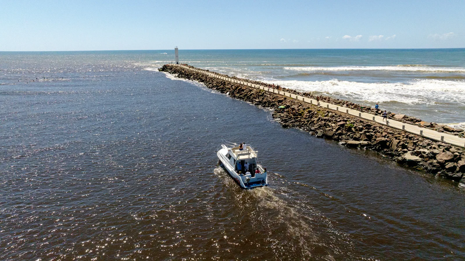 Vista aérea de un barco junto al camino de piedra y al faro de los Molhes da Barra