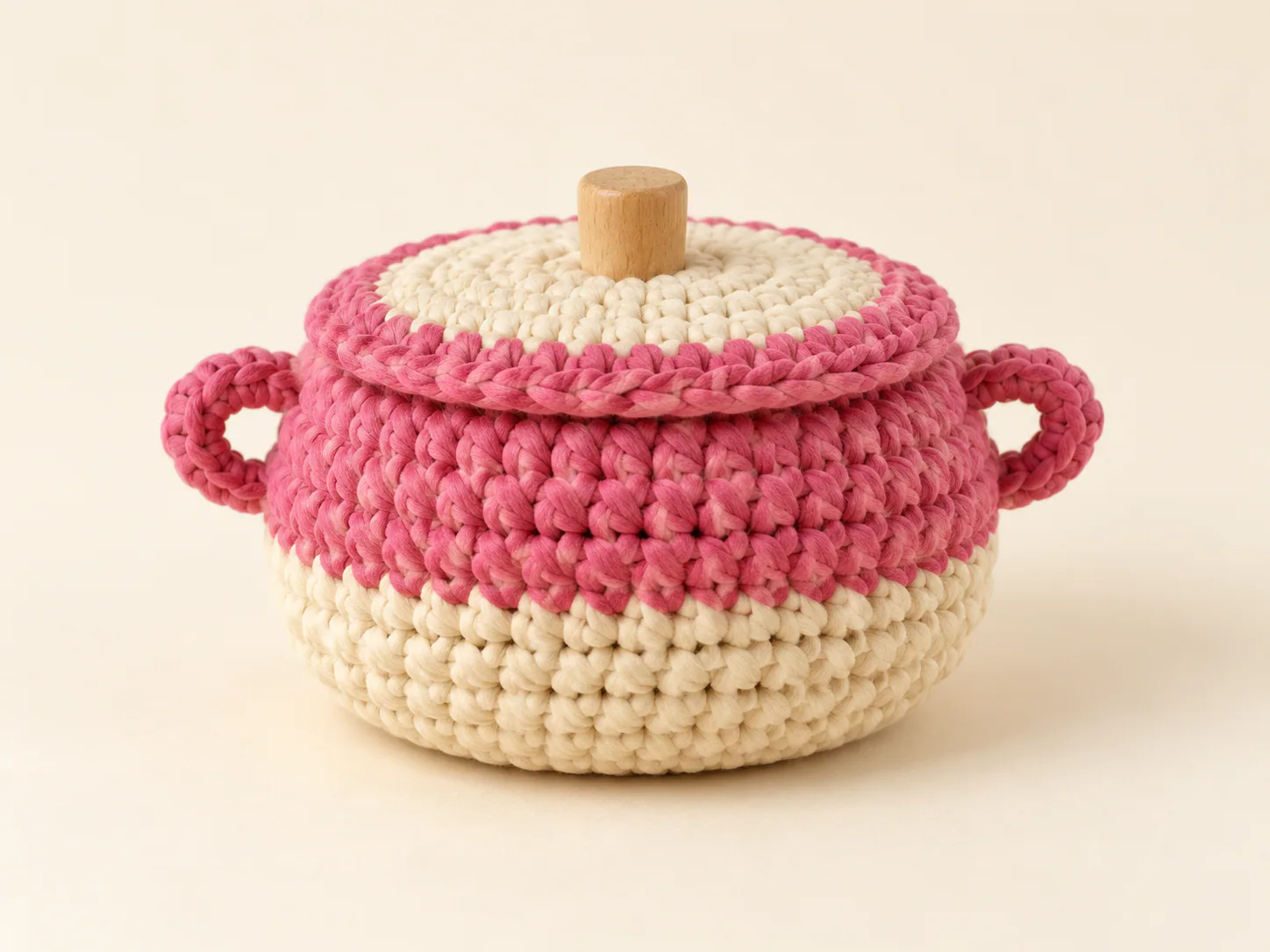 Cesto redondo de crochet en rosa y crudo, con asas laterales, tapa y pomo de madera.