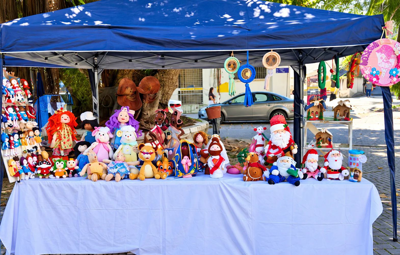Mesa con muñecos de tela y crochet, animales y piezas navideñas bajo una carpa azul.