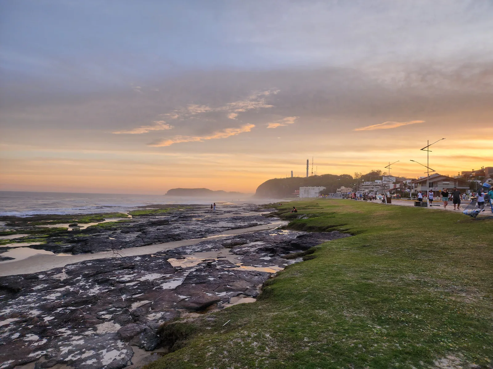 Rochas e gramados da Prainha ao entardecer, com o Morro do Farol ao fundo
