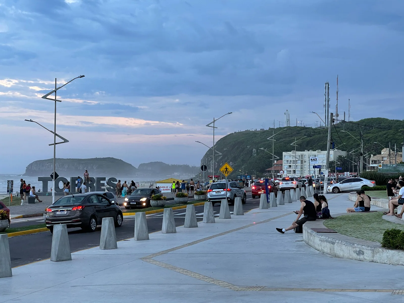 Pessoas passeando pela orla da Prainha, com o letreiro Torres ao fundo