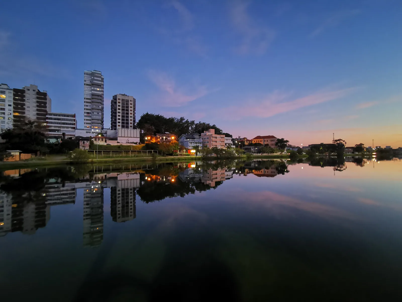 Reflexos das luzes dos prédios na Lagoa do Violão sob o céu rosado ao anoitecer