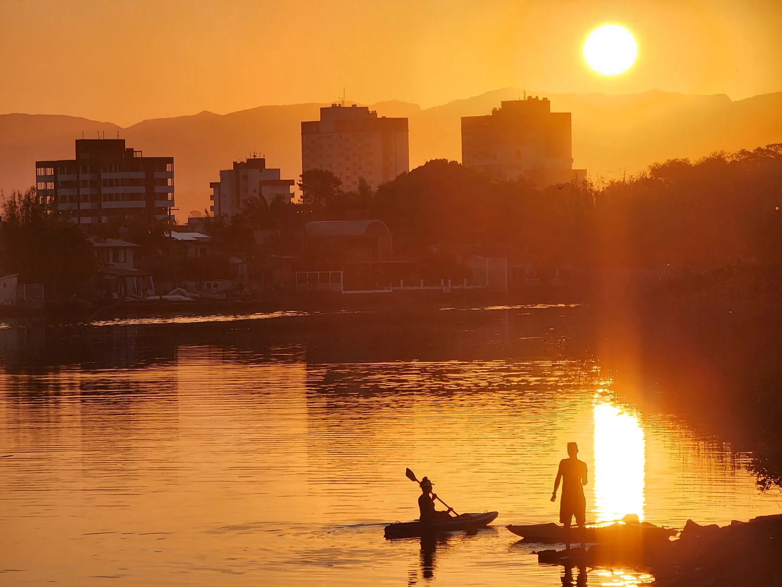 Caiaque e pessoas à margem do Rio Mampituba durante o pôr do sol