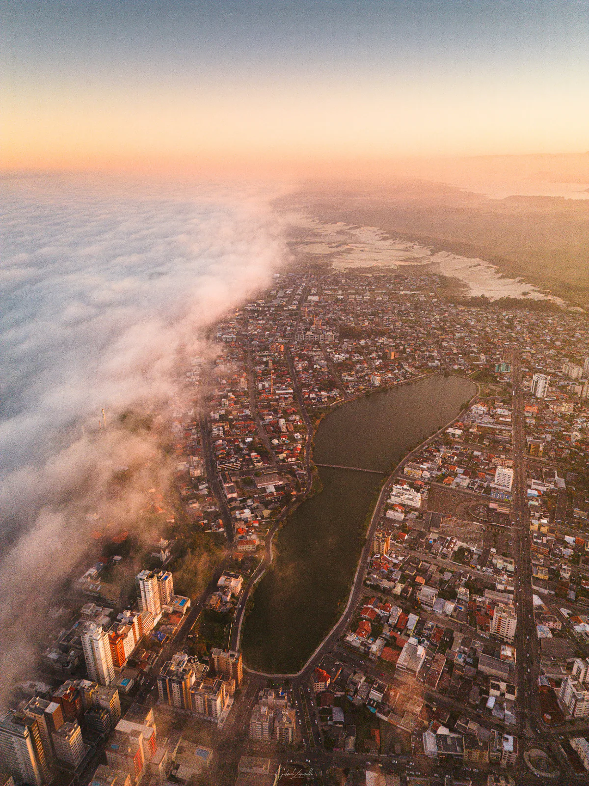 Vista aérea da Lagoa do Violão e da área urbana de Torres, com uma faixa de nuvens sobre a orla