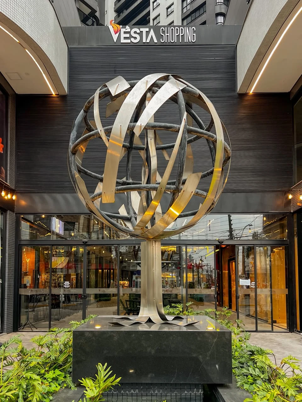 Esfera metálica de la escultura Munca sobre un pedestal, frente a Vésta Shopping.