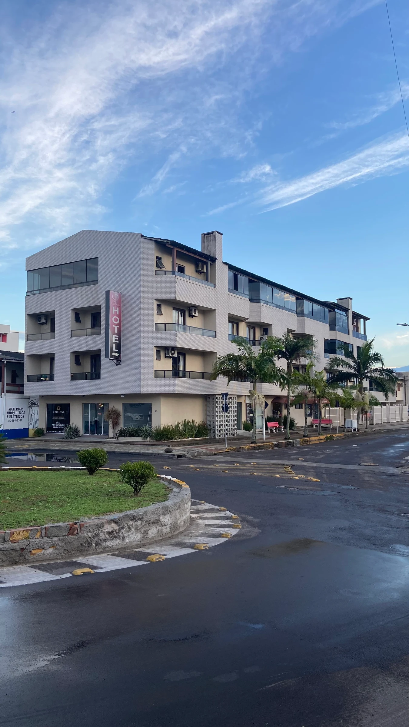 Fachada en esquina del Hotel Costa Dalpiaz, con balcones y palmeras frente a la entrada