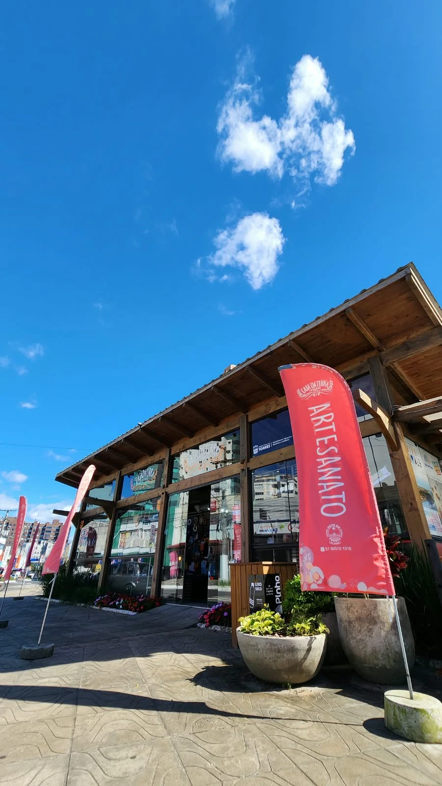 Timber and glass façade of Casa da Terra, with red banners and planters beside the entrance.