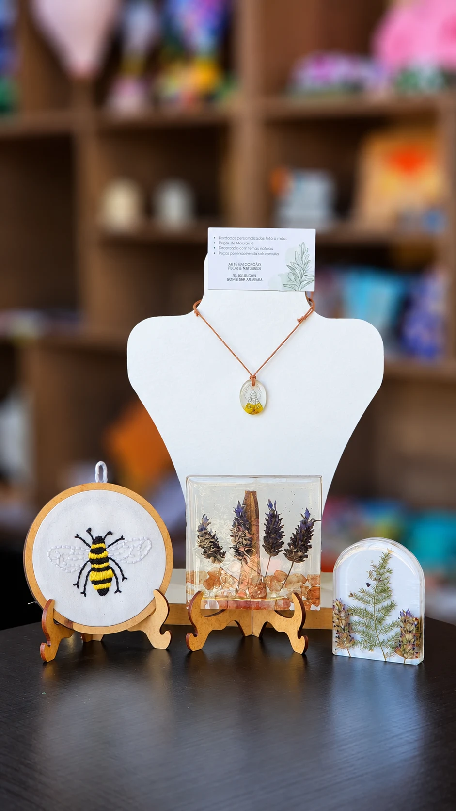 Necklace on a white display, an embroidered bee and clear decorative pieces containing plants.